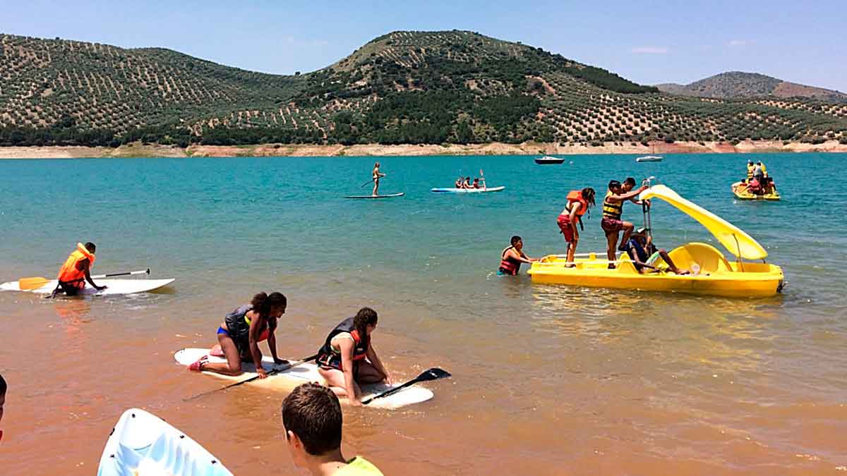 Personas disfrutando actividades acuáticas en la playa interior de Valdearenas, en el embalse de Iznájar, Córdoba, Andalucía