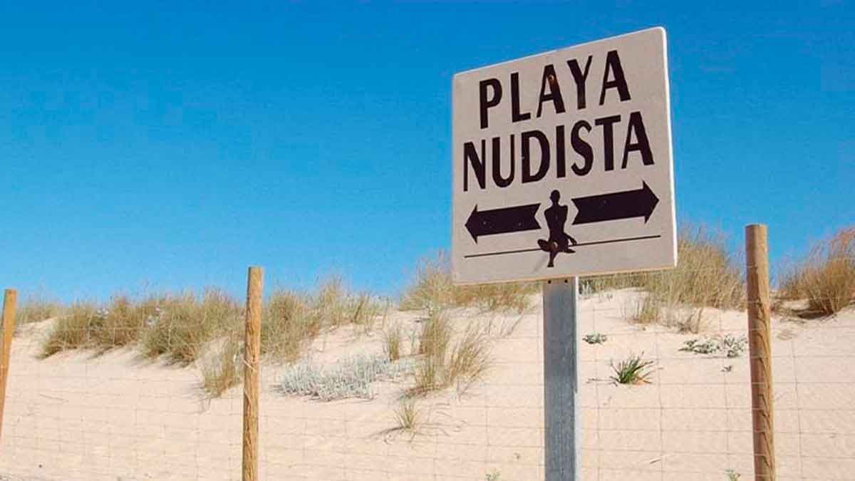 Cartel de playa nudista entre dunas de arena en la costa de Andalucía bajo un cielo completamente despejado
