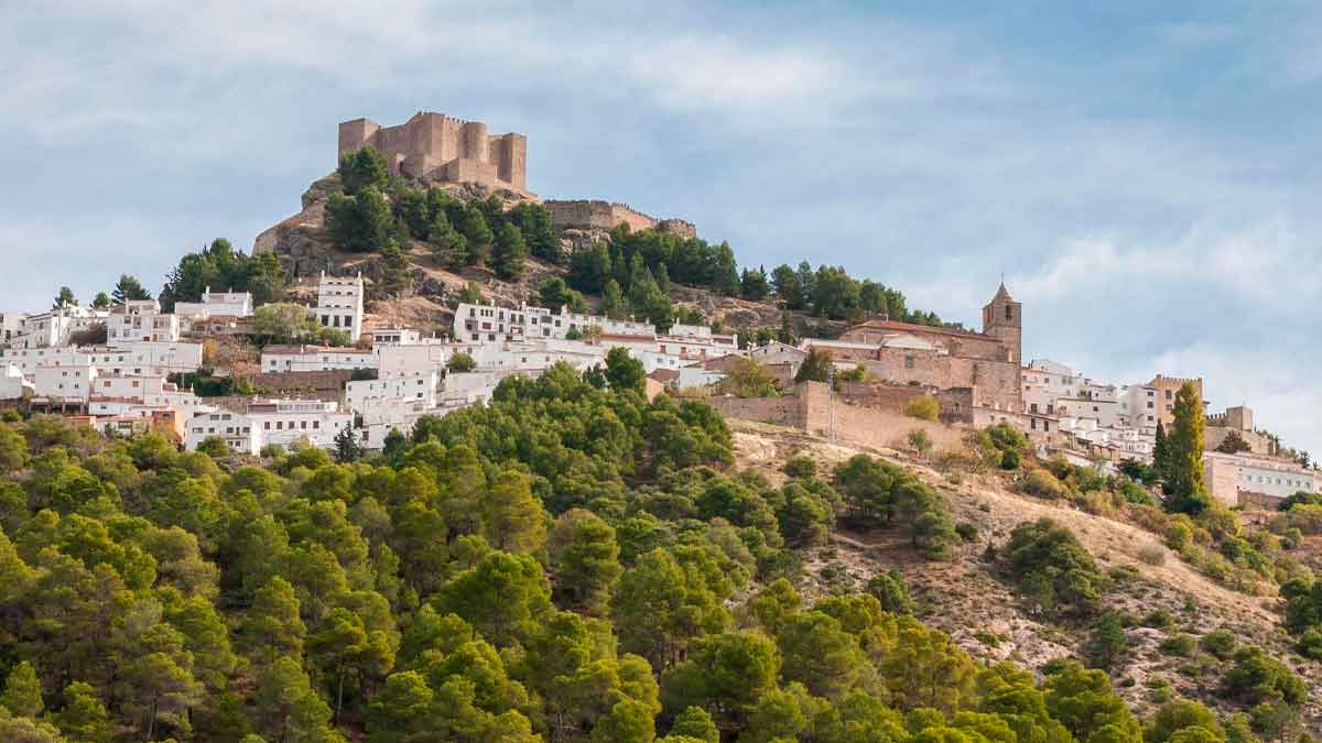 Vista de Segura de la Sierra con su castillo almohade sobre casas blancas y pinares; refugio andaluz ideal para un verano fresco