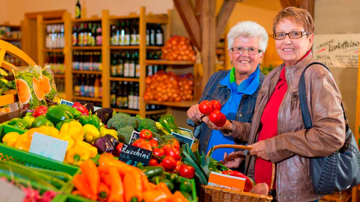 Dos personas mayores de 65 años eligiendo frutas y verduras saludables en un supermercado para mejorar energía y sueño