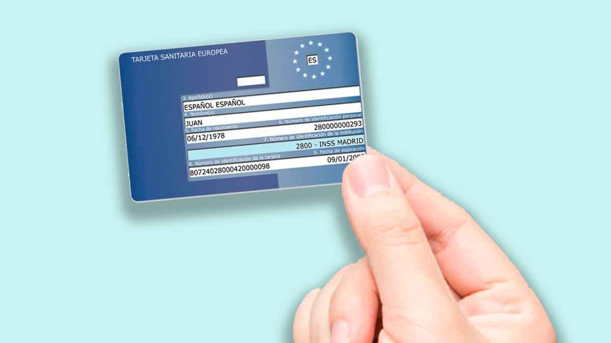 Mano sosteniendo una Tarjeta Sanitaria Europea azul sobre fondo celeste, documento que puedes recibir en cinco días tras solicitarlo online