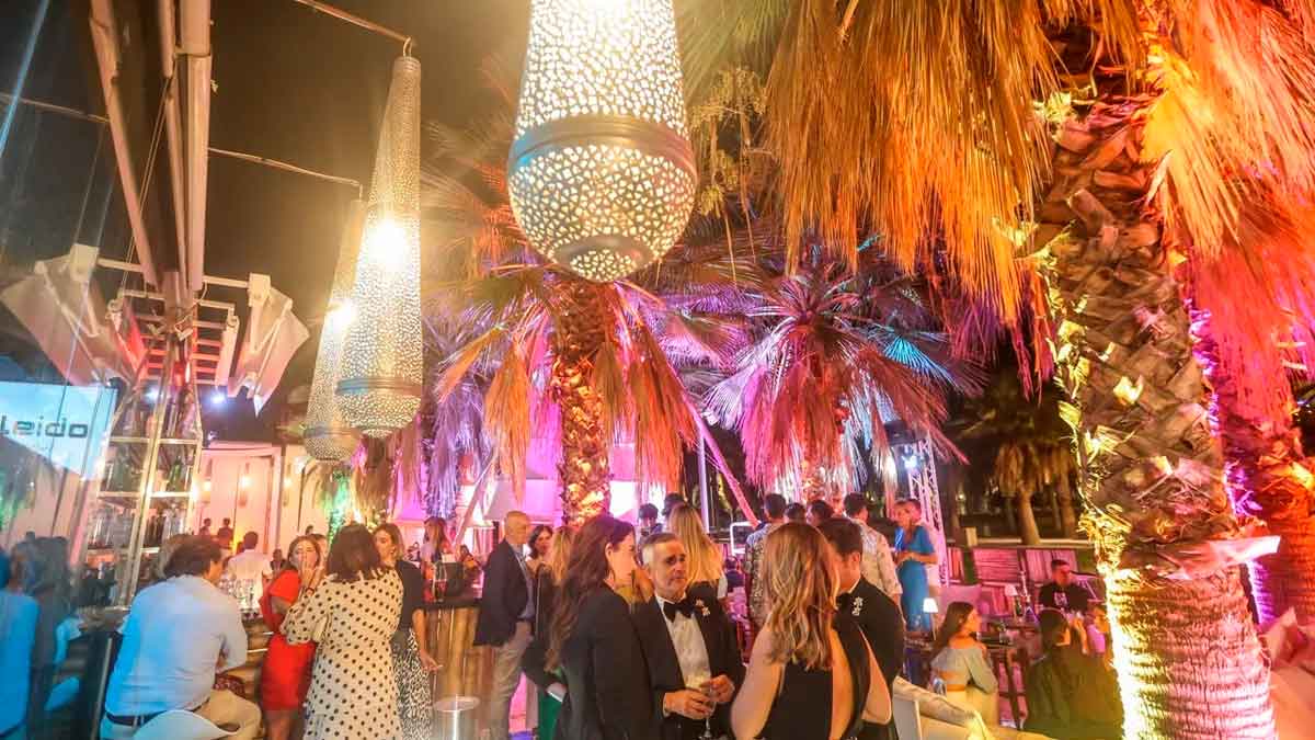 Terraza nocturna en Málaga con ambiente exclusivo, iluminación elegante y clientes disfrutando de cócteles en un entorno tropical