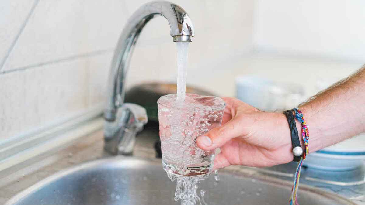 Persona llenando un vaso de agua en el fregadero para evitar malos olores en la cocina durante vacaciones