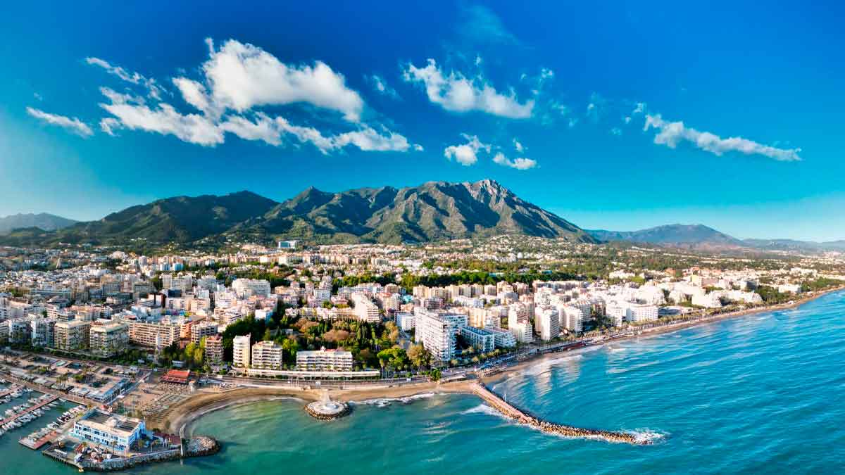 Vista aérea de Marbella en la Costa del Sol con la playa, la ciudad y la Sierra Blanca al fondo, destino más caro para alquilar apartamento en verano 2025