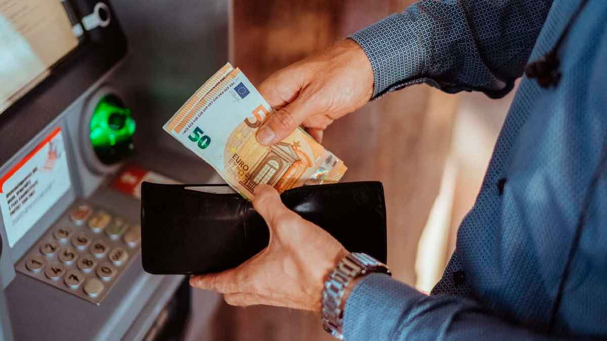 Persona retira billetes de 50 euros de un cajero automático, ilustrando el cobro del paro correspondiente a agosto de 2025
