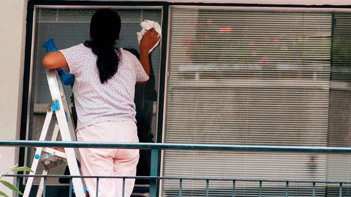 Empleada del hogar limpiando ventanas tras lograr indemnización por despido improcedente reconocida por la Justicia en Asturias