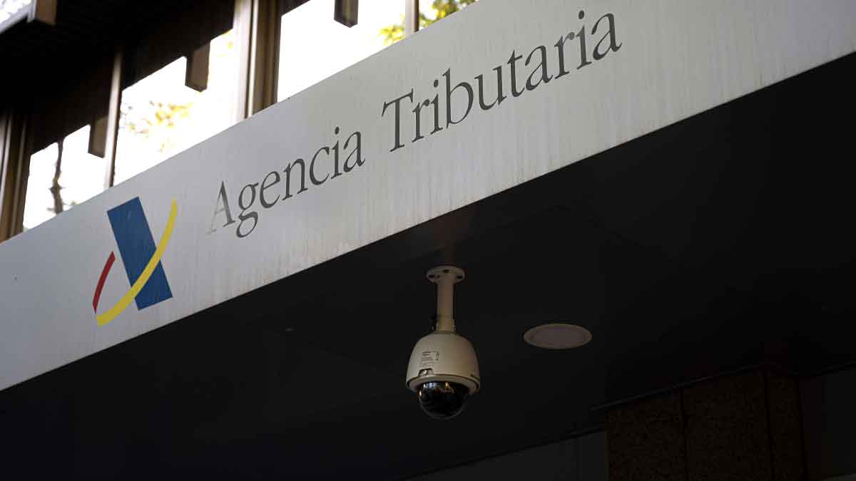 Entrada de la Agencia Tributaria con su logotipo y una cámara de seguridad, relacionada con las implicaciones fiscales de añadir a un hijo como cotitular de la cuenta bancaria