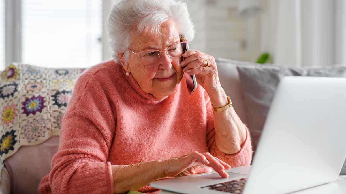 Mujer mayor hablando por teléfono y usando ordenador para evitar estafas telefónicas