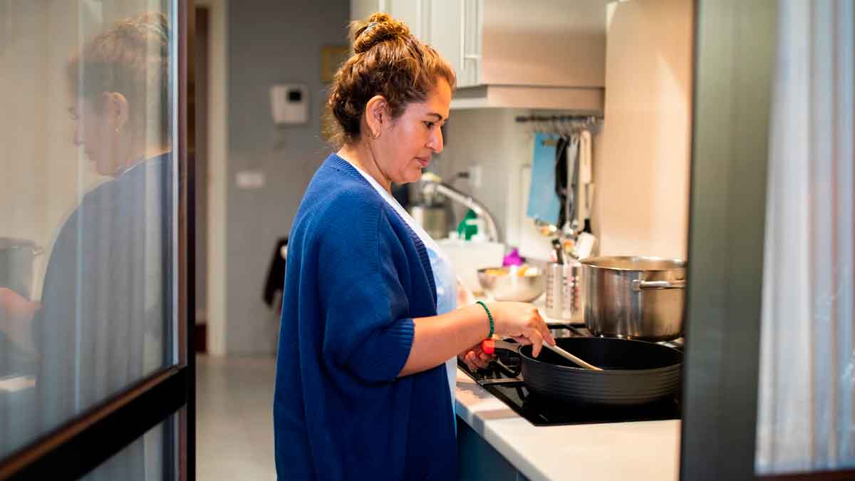 Mujer empleada de hogar cocinando en una cocina, relacionada con subsidio para mayores de 52 años