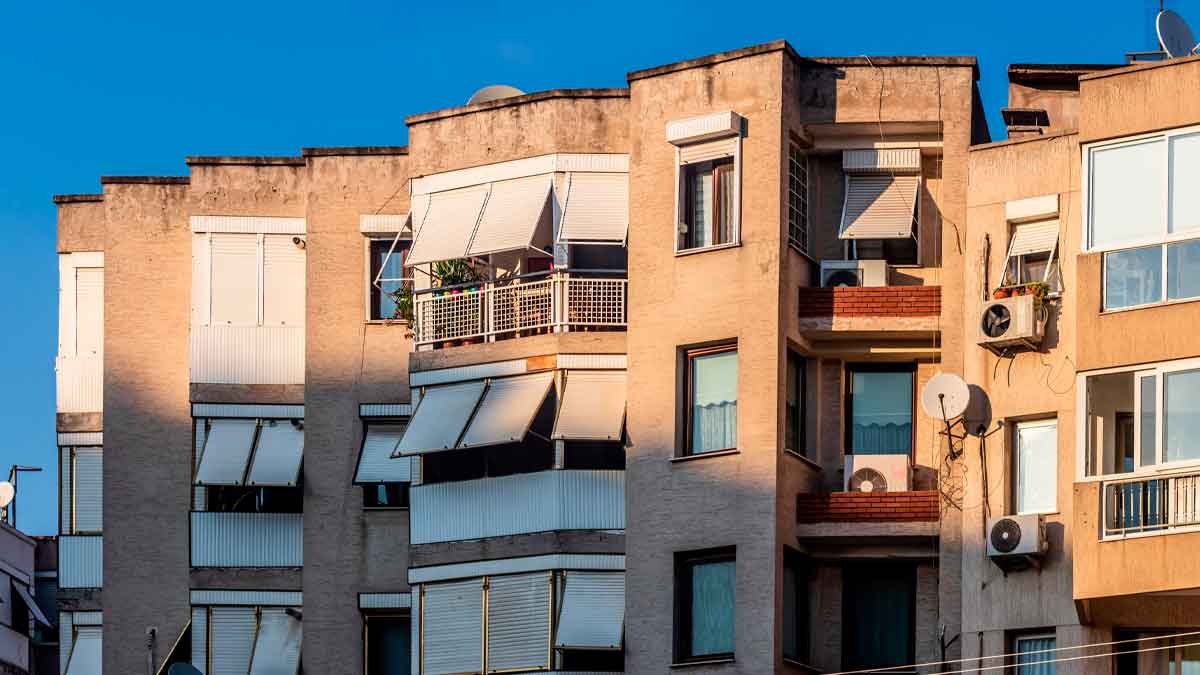 Fachada de edificio de viviendas antiguas con toldos, aparatos de aire acondicionado y persianas, ejemplo de inmueble que debe mejorar a clase energética E antes de 2030 en España