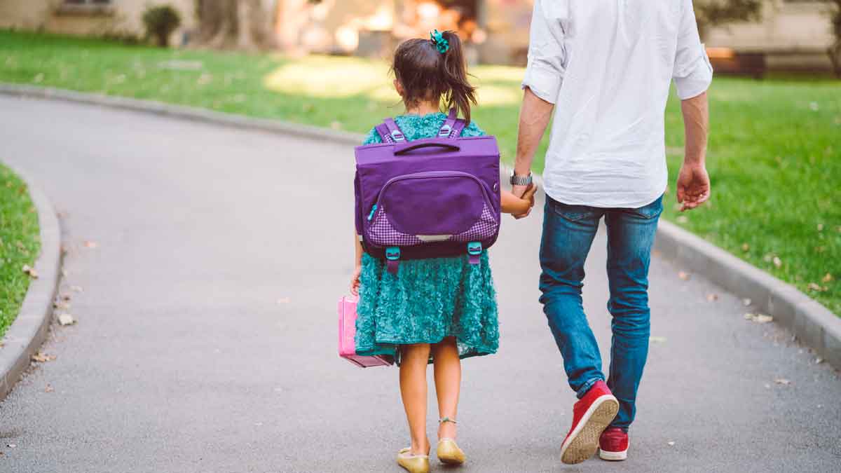 Niña con mochila volviendo al colegio acompañada de su padre en la vuelta al cole 2025-2026