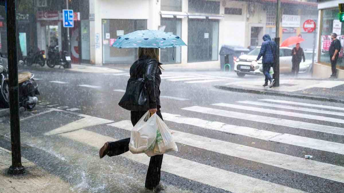 Personas con paraguas caminan bajo fuerte lluvia en Andalucía durante la alerta amarilla de AEMET por tormentas