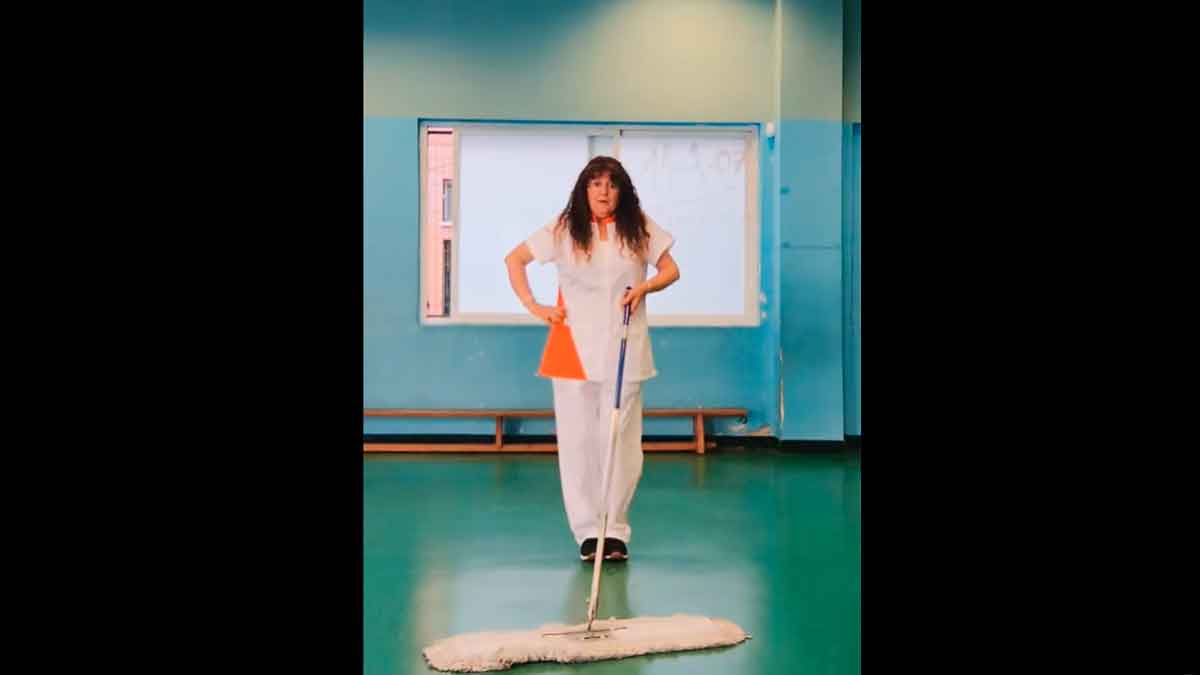 Limpiadora con uniforme blanco bailando con una mopa en un centro de trabajo