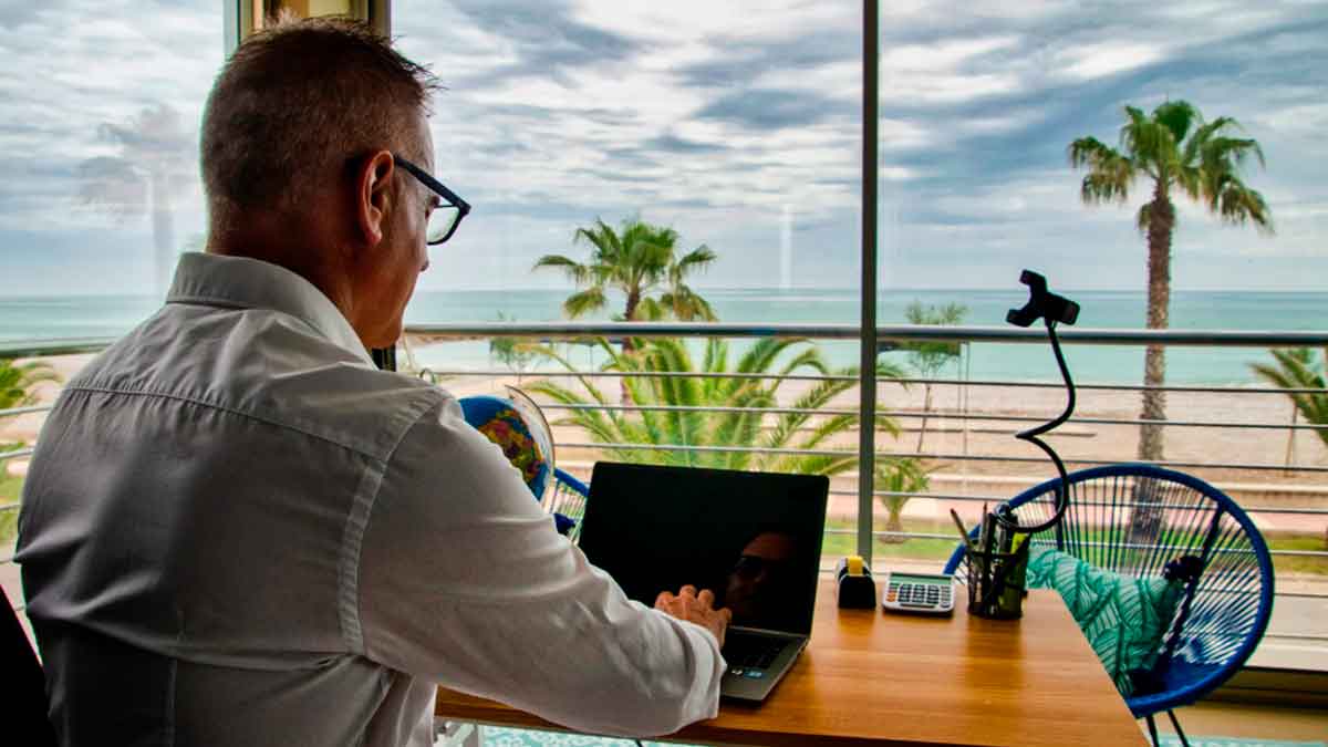 Hombre teletrabajando con portátil frente al mar en una oficina improvisada