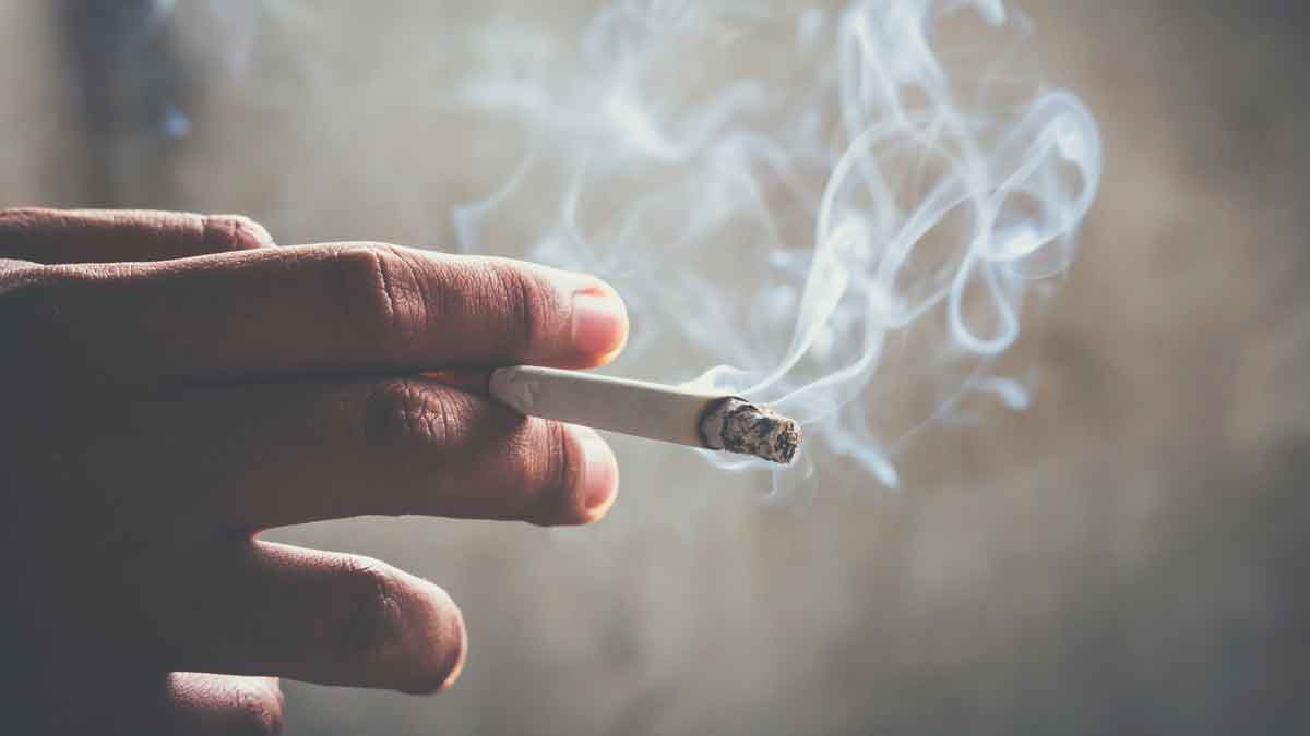 Mano sosteniendo cigarrillo encendido con humo relacionado con la nueva ley antitabaco