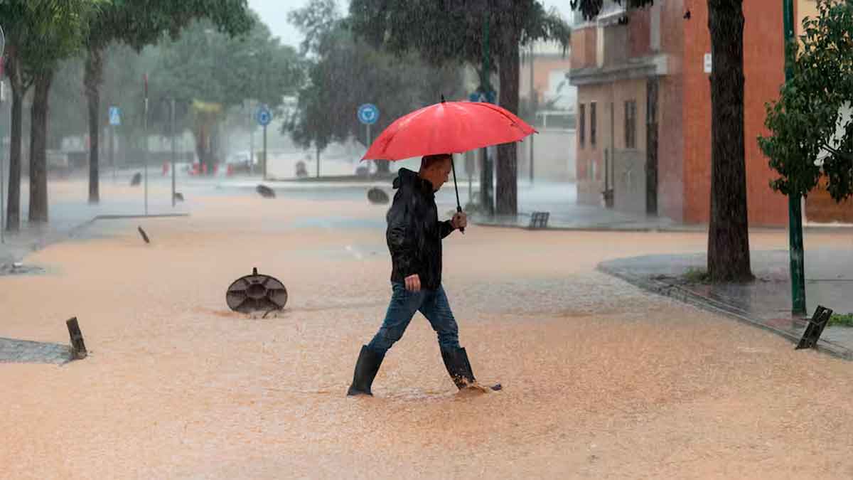 Hombre con paraguas rojo caminando por calle inundada durante lluvias torrenciales en España