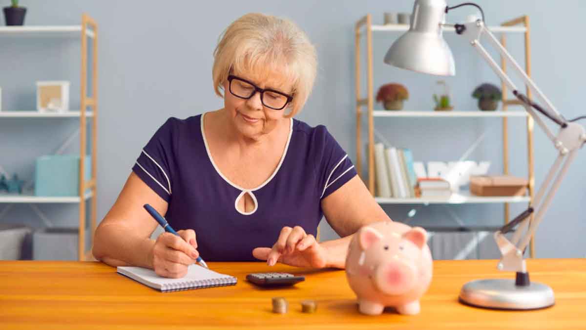 Mujer pensionista haciendo cuentas en casa con una hucha y calculadora por la subida de pensiones en 2026