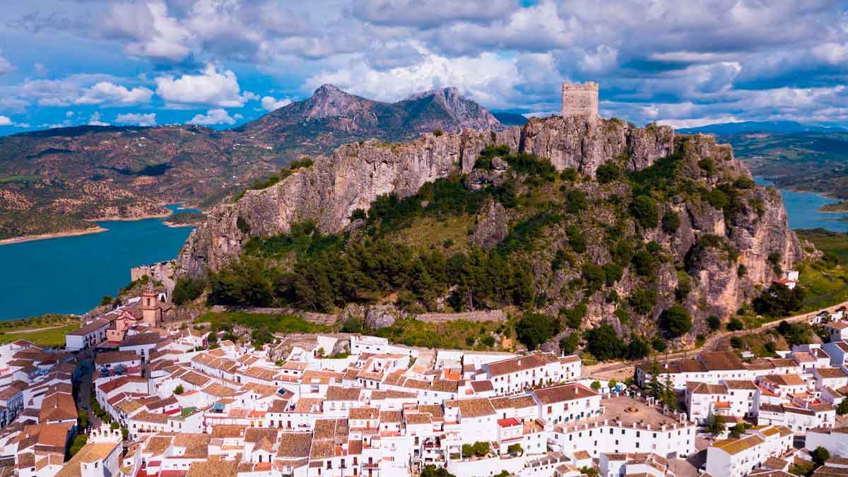 Vista panorámica de un pueblo blanco andaluz con castillo medieval y casas encaladas junto a un embalse