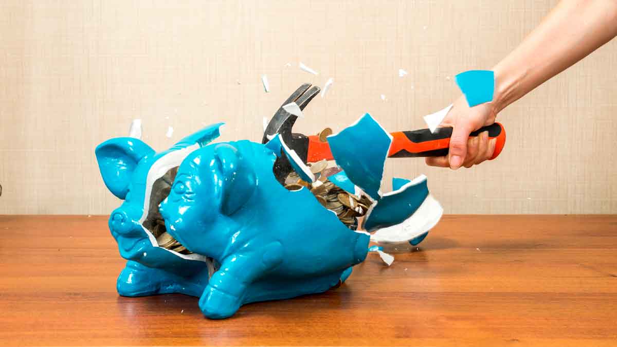 Hucha azul rota con martillo para simbolizar ahorro y regla 50 30 20 en la cuesta de septiembre