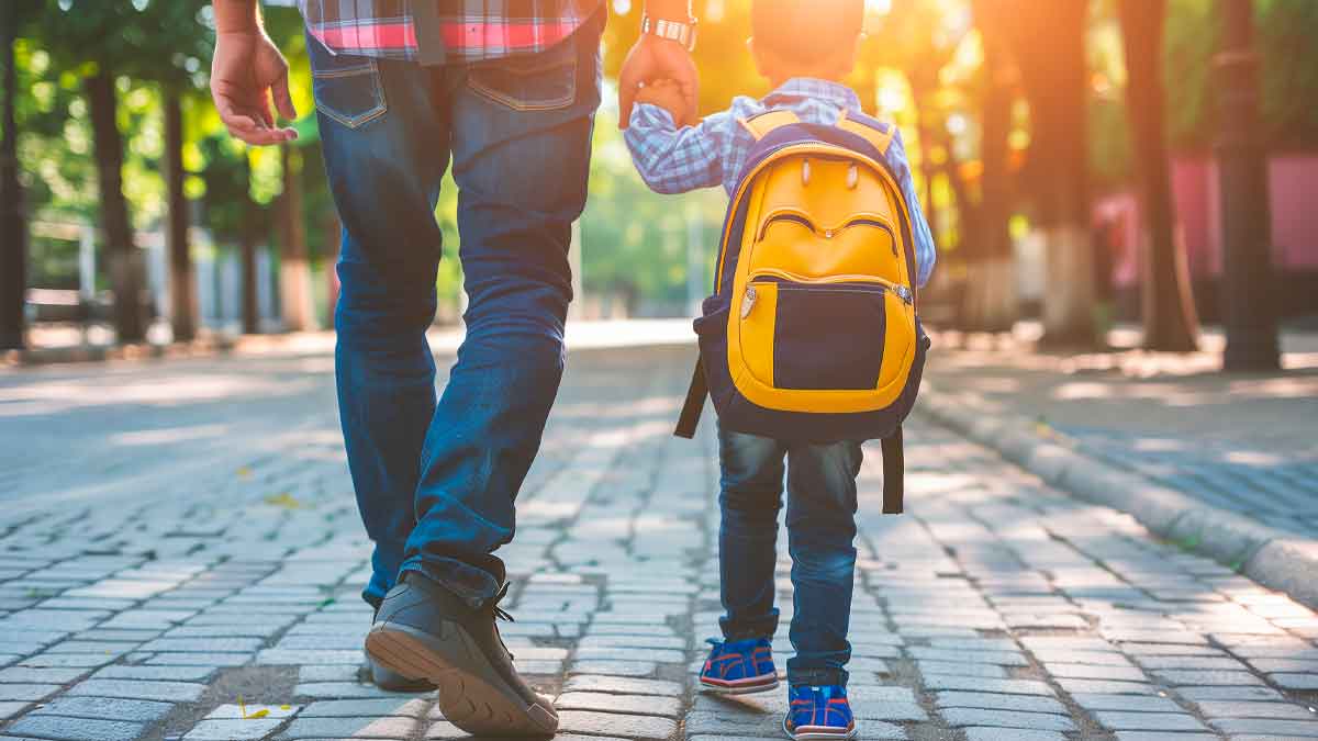 Padre llevando a su hijo al colegio con mochila amarilla durante la vuelta al cole en septiembre 2025 en España