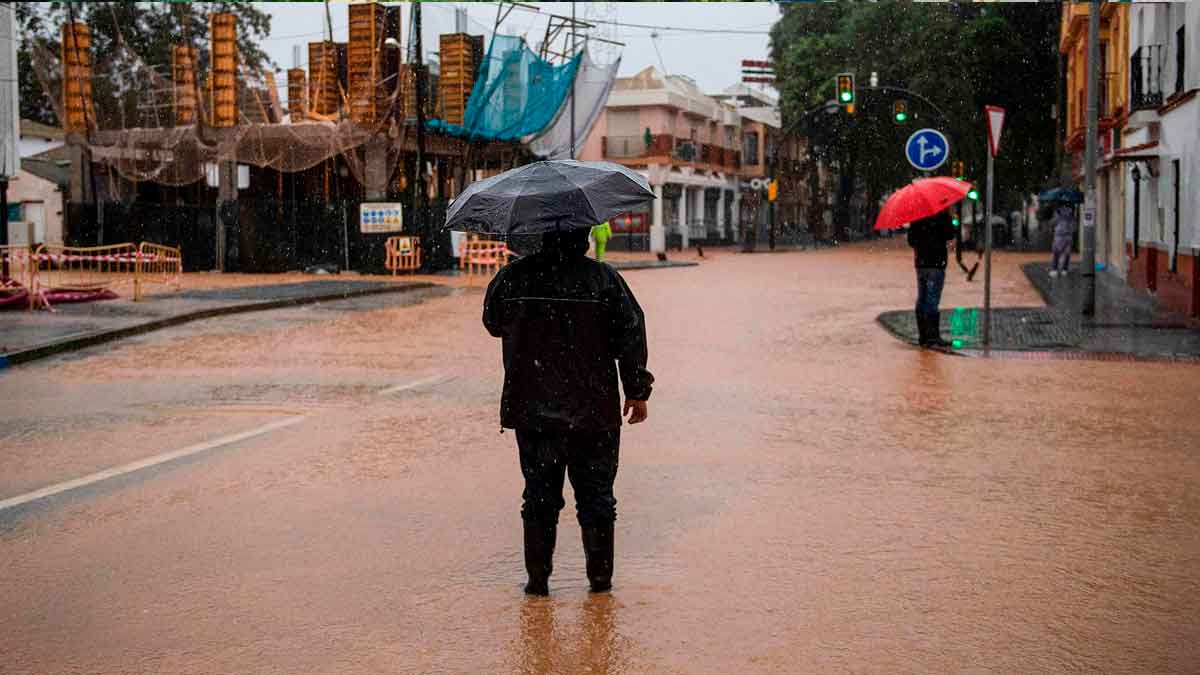 Personas con paraguas caminando por una calle inundada en Andalucía durante el aviso naranja por lluvias intensas