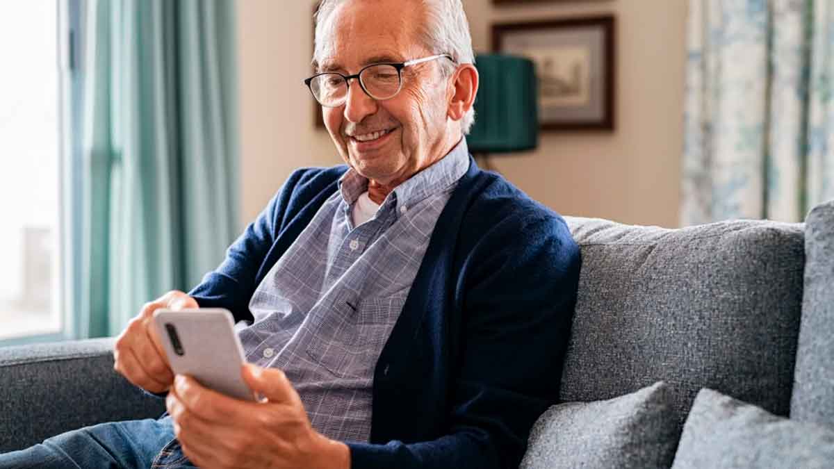Pensionista mayor consultando su pensión desde el móvil en casa tras la subida del IPC en 2026