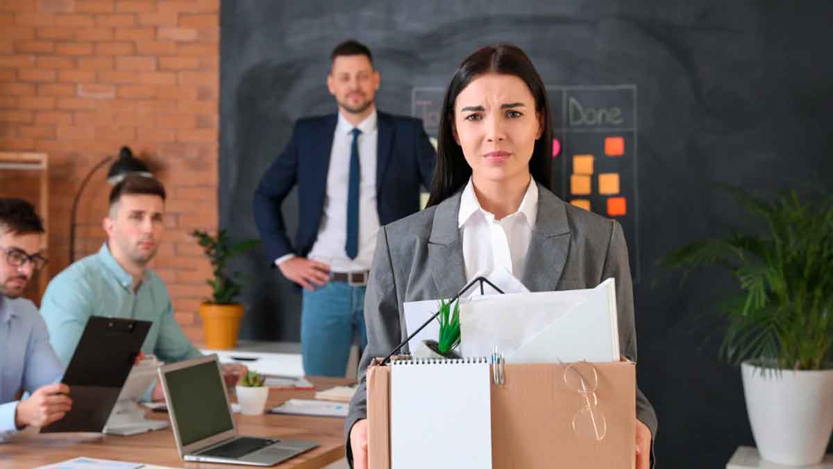 Mujer con caja de pertenencias tras ser despedida en una oficina junto a compañeros de trabajo