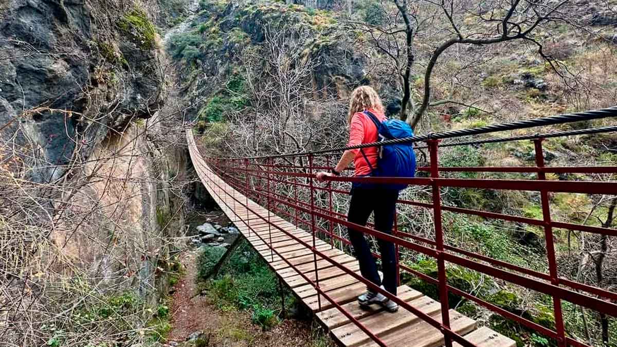 Persona cruzando un puente colgante en la ruta de senderismo fácil de los Cahorros de Monachil en otoño, Granada, Andalucía