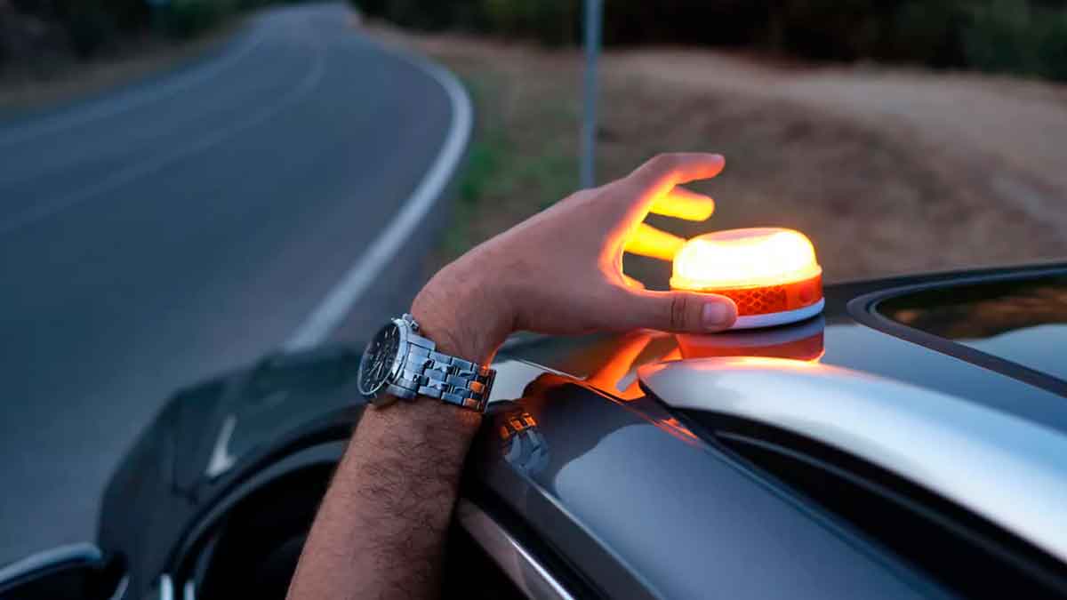 Conductor colocando una luz V16 conectada homologada por la DGT sobre el coche para señalizar una avería en carretera