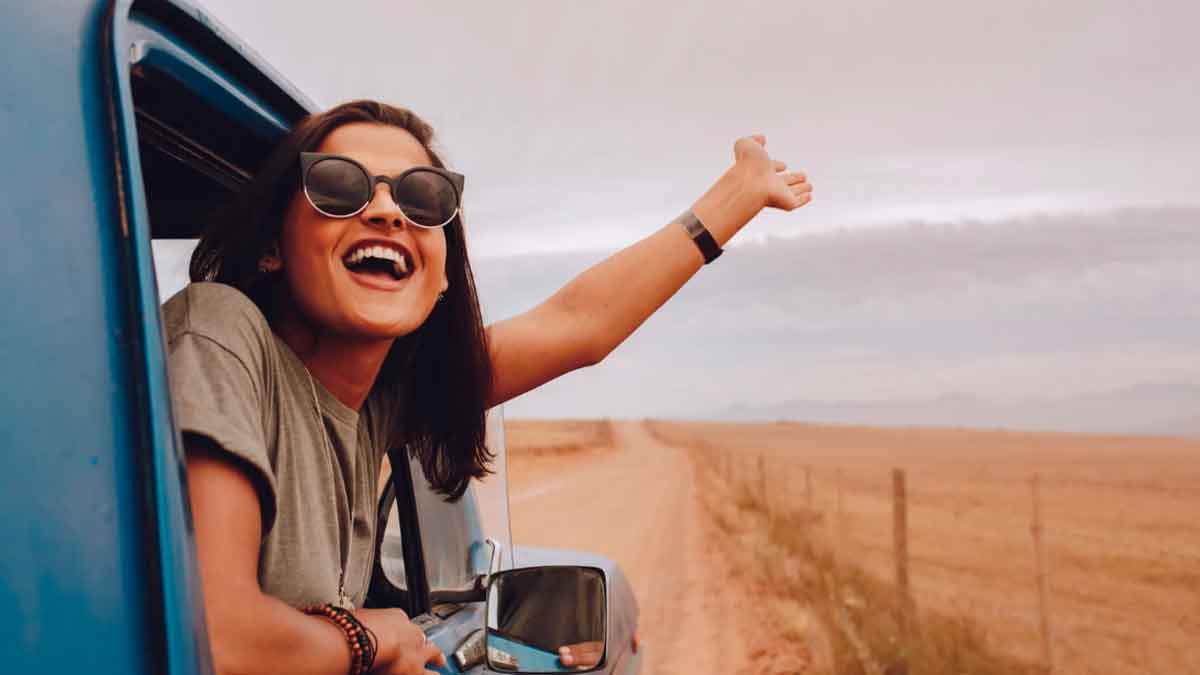 Joven asomada a la ventanilla de un coche disfrutando de un viaje por una carretera rural