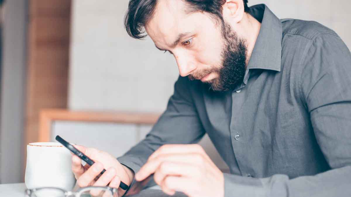 Hombre revisando su app bancaria en el móvil con dificultades para cerrar una cuenta según la OCU