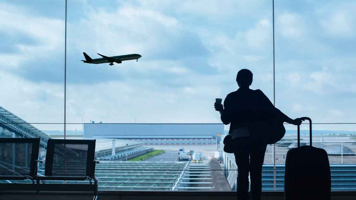Persona con maleta observando un avión despegar desde la terminal de un aeropuerto