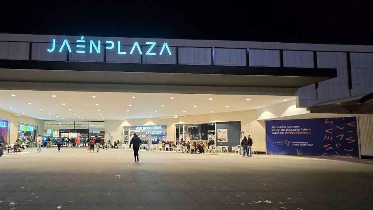 Entrada principal del centro comercial Jaén Plaza iluminada por la noche con personas accediendo al recinto
