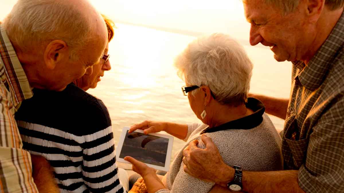 Personas mayores jubiladas disfrutando juntas mientras consultan información en una tableta sobre sus derechos y pensión