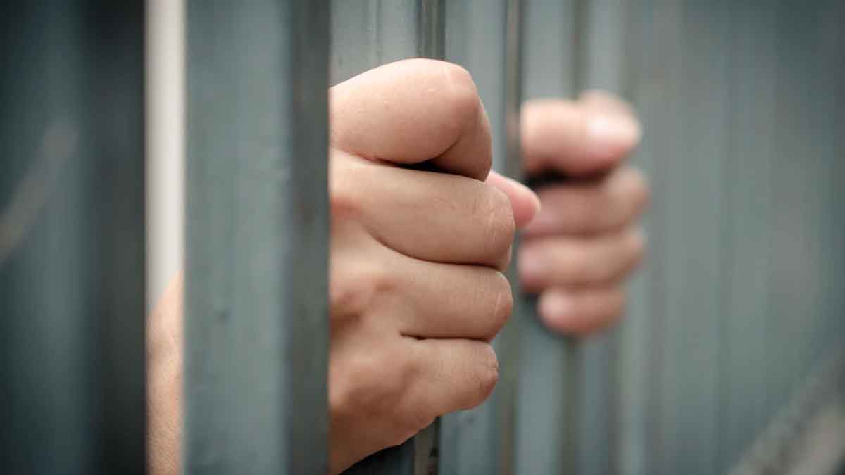 Manos sujetando barrotes de prisión en referencia a un trabajador despedido por ausencias injustificadas