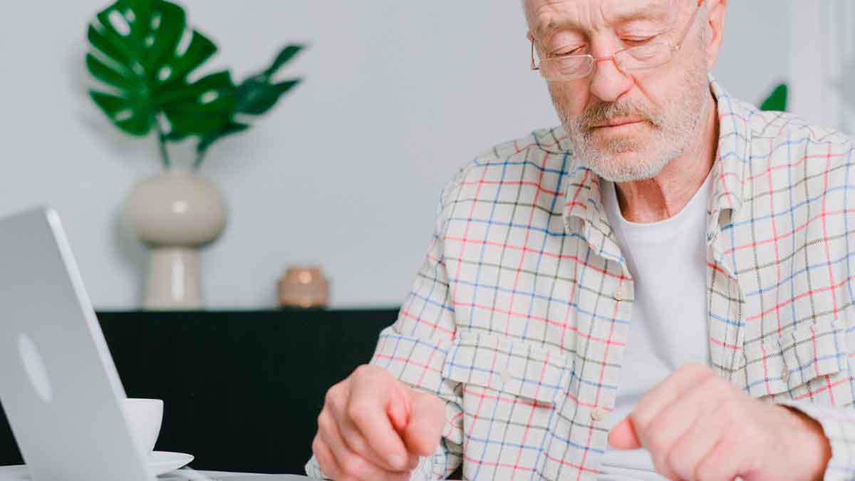 Hombre mayor revisando documentos frente al ordenador en un entorno doméstico