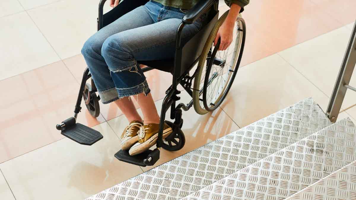 Persona en silla de ruedas frente a unas escaleras que necesita obras de accesibilidad en una comunidad de vecinos