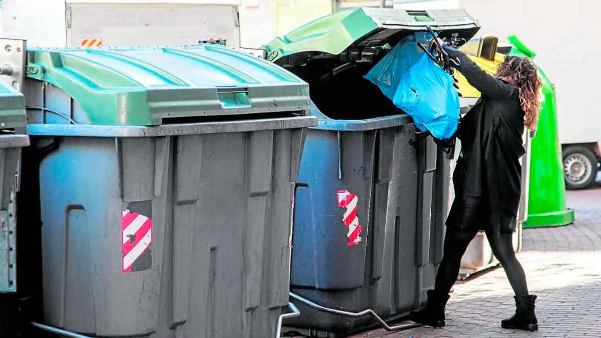 Persona depositando una bolsa de basura en un contenedor urbano de residuos en una calle de la ciudad