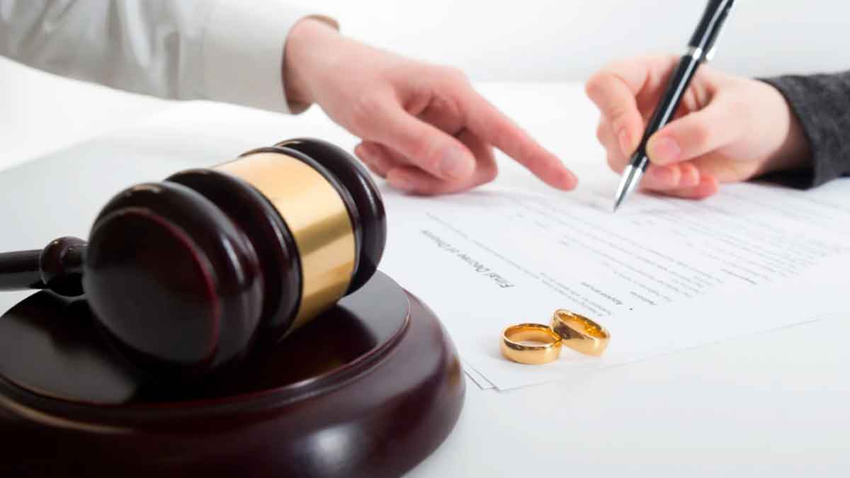 Firma de documentos de divorcio junto a anillos de boda y mazo judicial, símbolo de pensión de viudedad