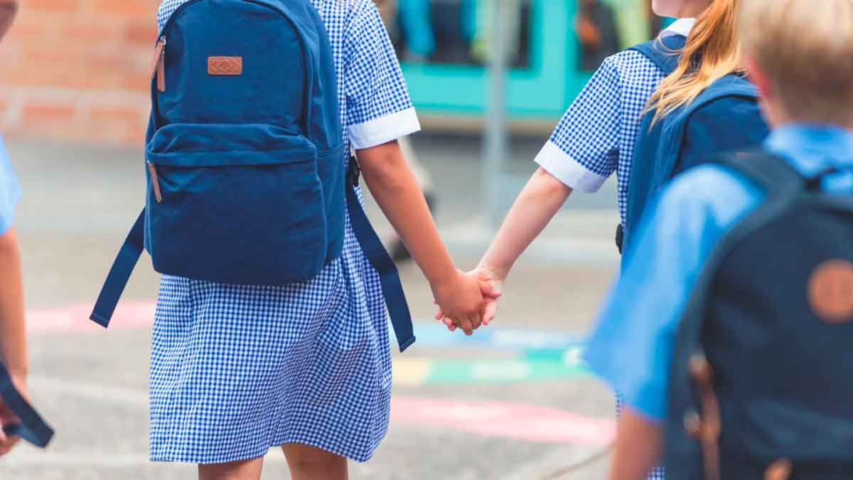 Niños con mochilas escolares caminando juntos de la mano en su centro educativo