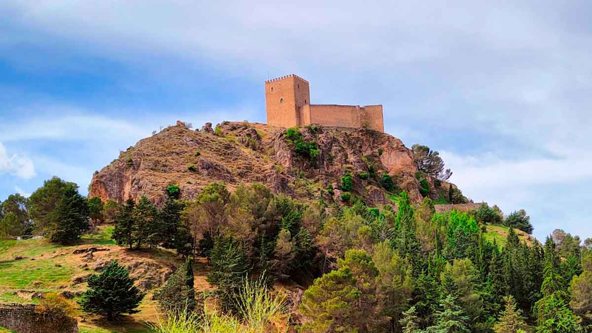 Castillo medieval en lo alto de una colina rodeado de naturaleza en Andalucía, parte de la ruta de los castillos andaluces