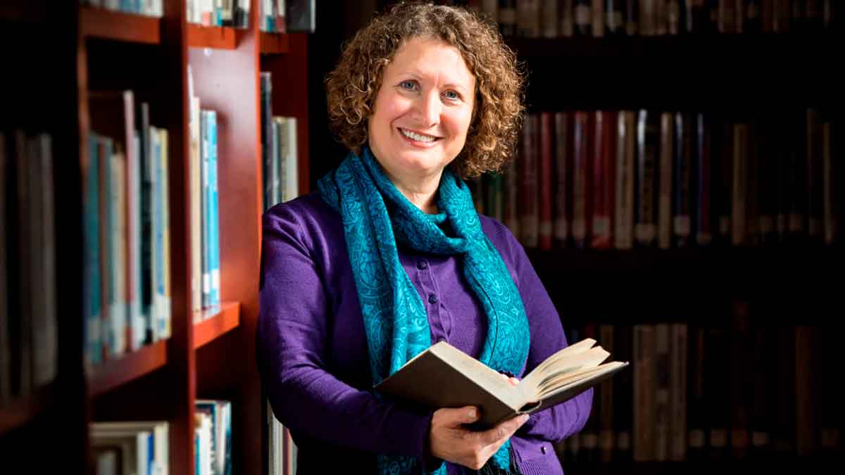 Bibliotecaria leyendo un libro en una biblioteca para noticia sobre plazas de técnico auxiliar en la Universidad de Cádiz