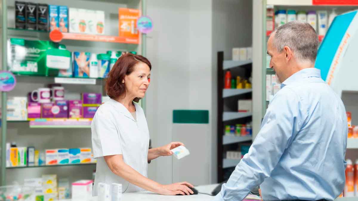 Farmacéutica atendiendo a un paciente en una farmacia andaluza durante renovación de tratamientos crónicos
