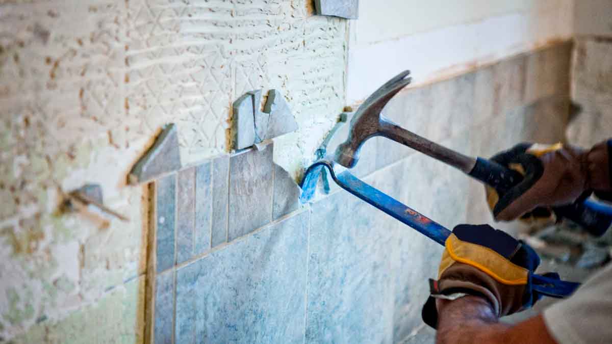Mano retirando azulejos durante obras en una vivienda de una comunidad de vecinos