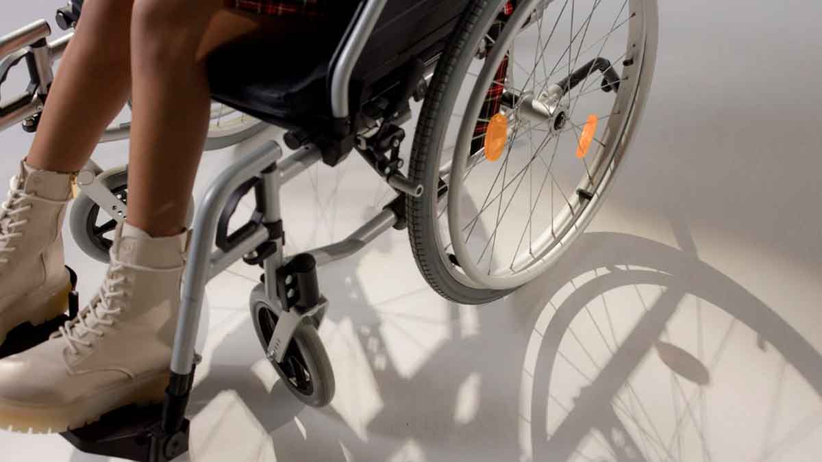 Persona sentada en una silla de ruedas con botas claras y luz proyectando la sombra del dispositivo