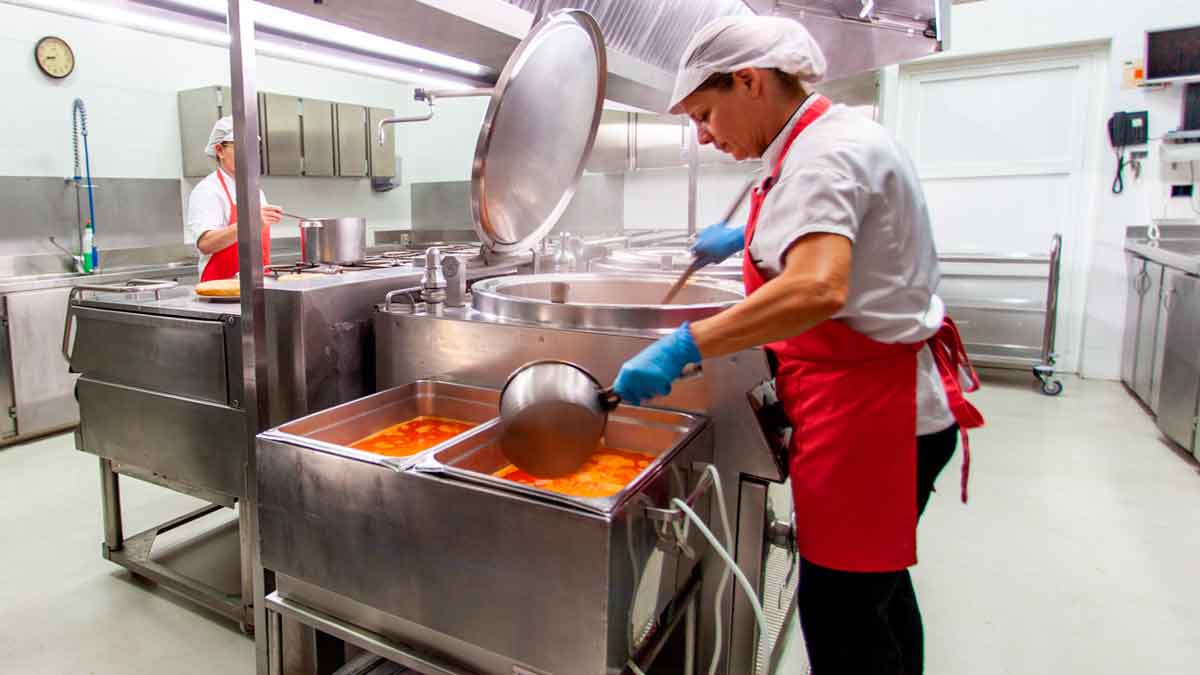 Trabajadora de cocina preparando alimentos en una cocina industrial durante su jornada laboral