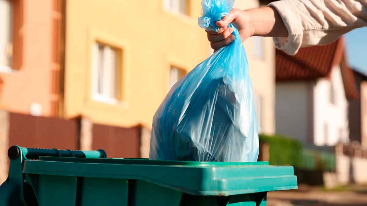 Persona depositando una bolsa de basura en un contenedor en un entorno urbano